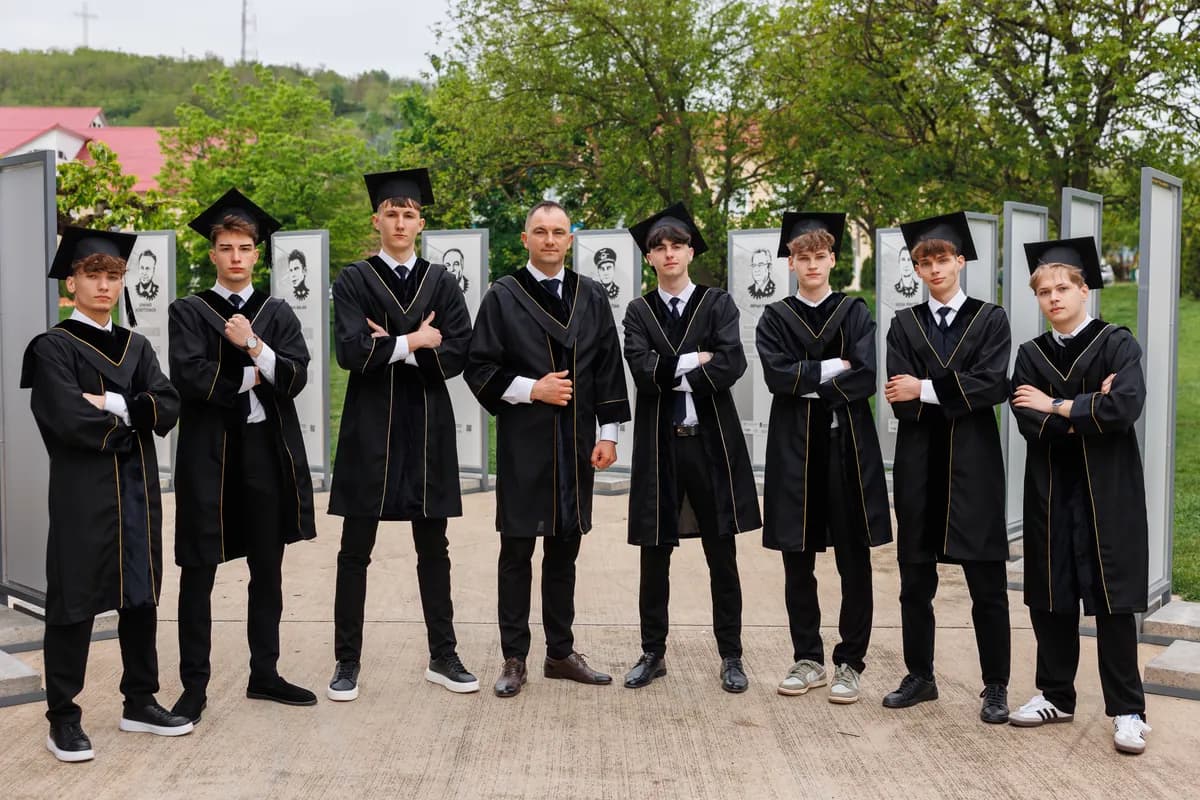 Fotografie de grup cu absolvenți în mantii negre, în aer liber